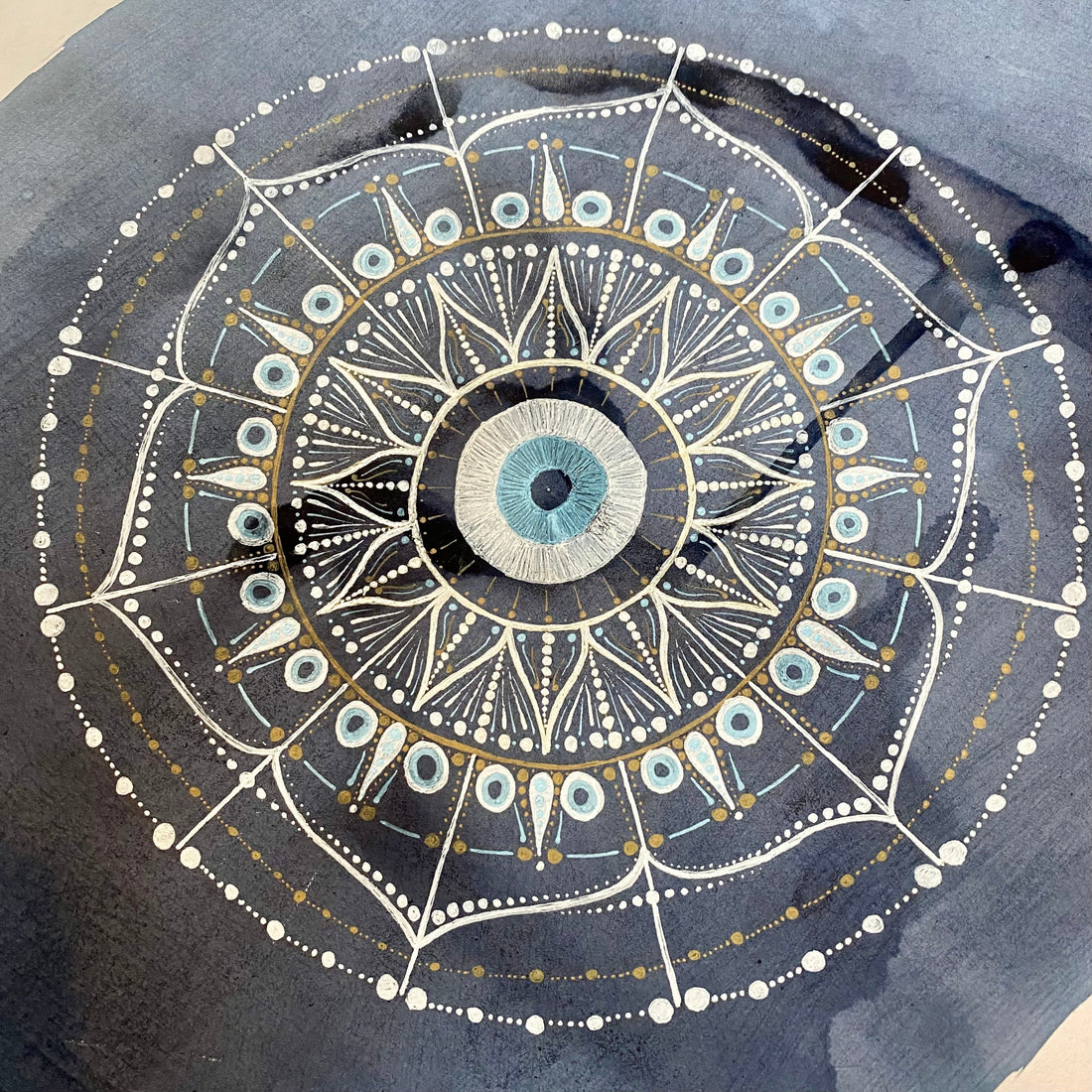 Mandala with an evil eye at it's centre, drawn in white and pale blue gel pens on a background of dark blue elderberry ink