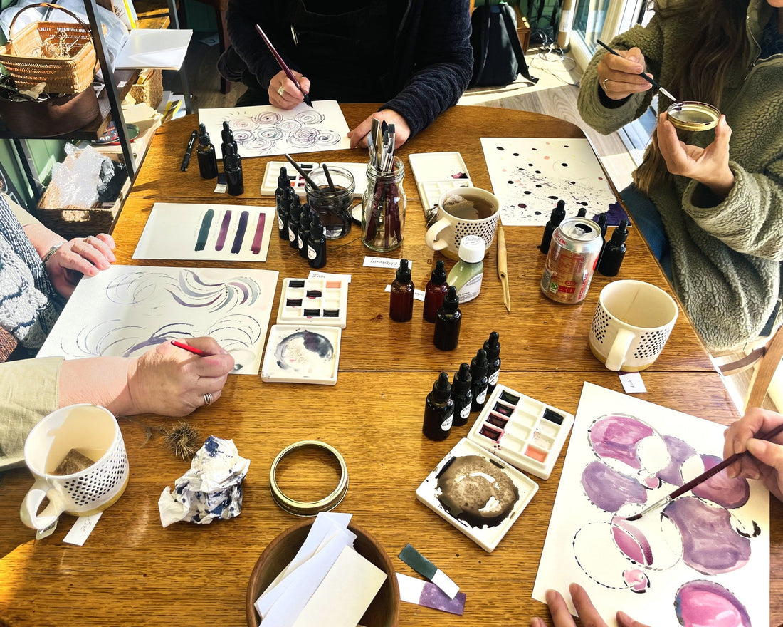 The table mid-workshop at Tree to Ink: elderberry ink bottles, swatches in green, purple and pink, stamped circles and spirals