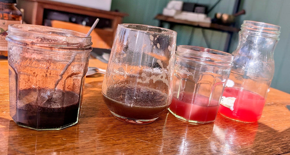 Four jars of rowan berry ink on the table, from dark brown to coral pink, against the green studio wall