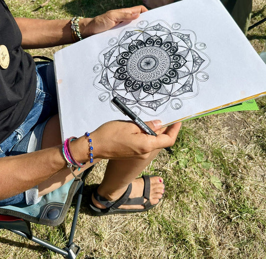 Louise drawing a mandala in a camp chair outdoors, pen in hand, the circle half finished